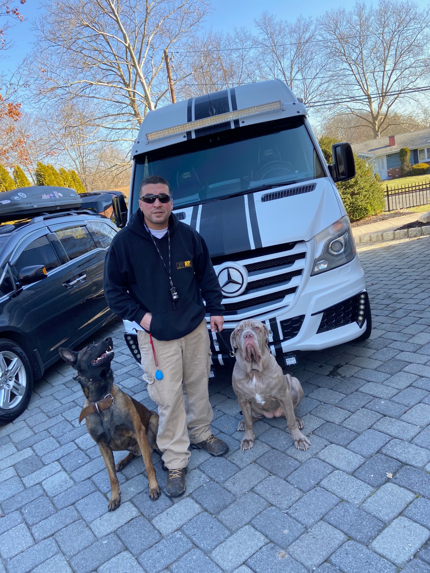 ACT K9 trainer with a Malinois and a cane corso seated calmly in front of the training van
